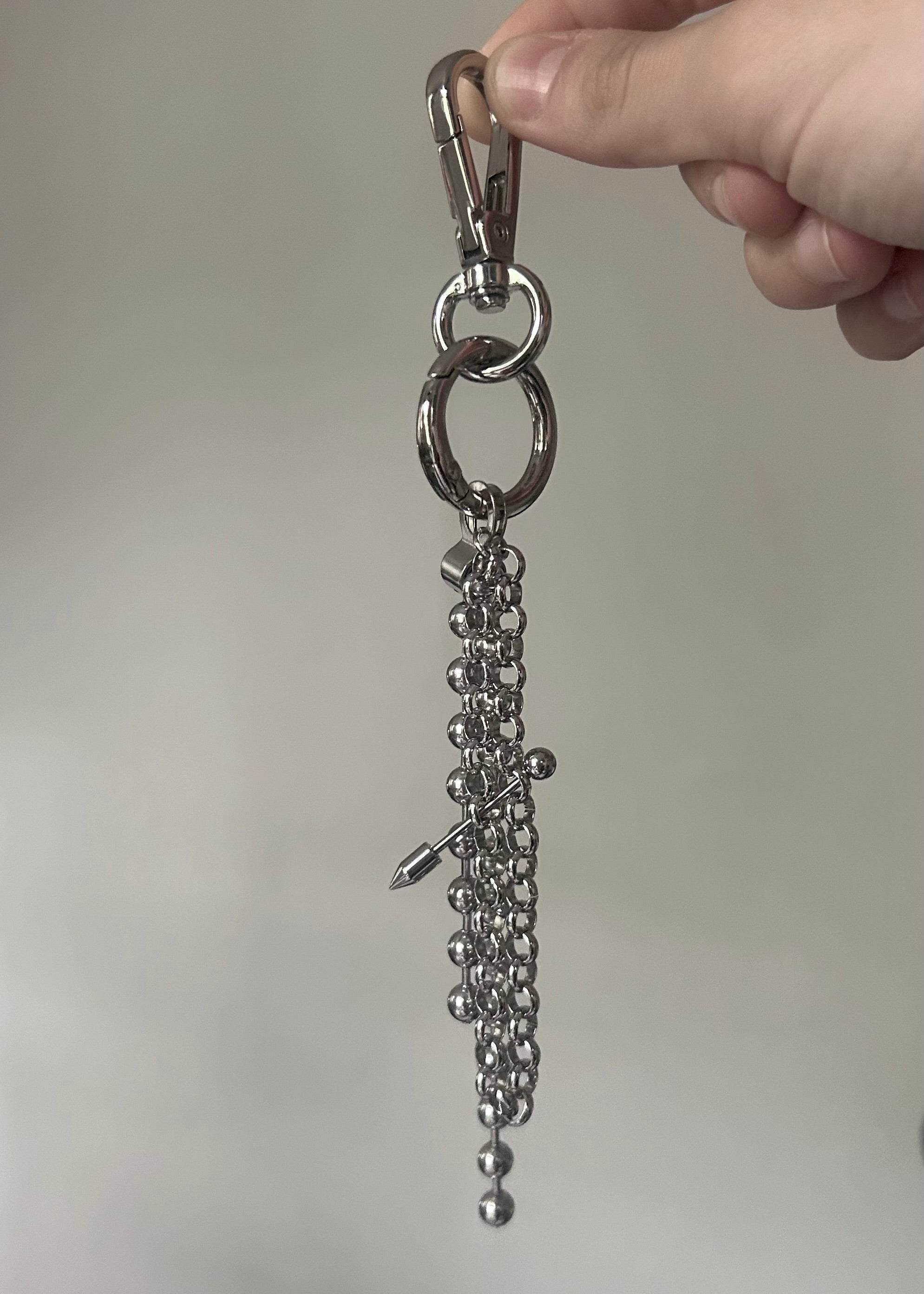 Metal keychain with beads and a clasp held by a hand against a neutral background