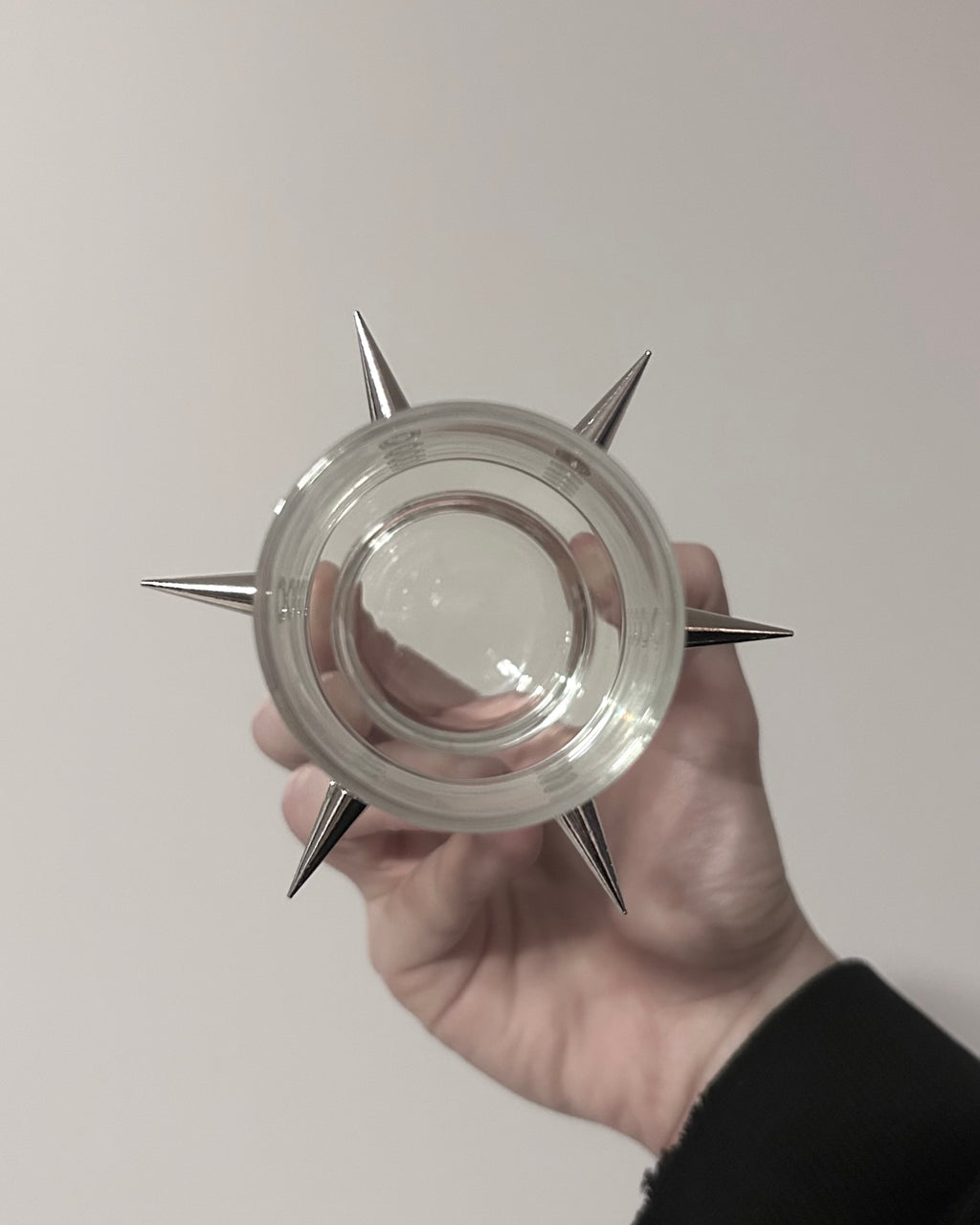 Clear glass container with metallic spikes held in a hand against a plain background
