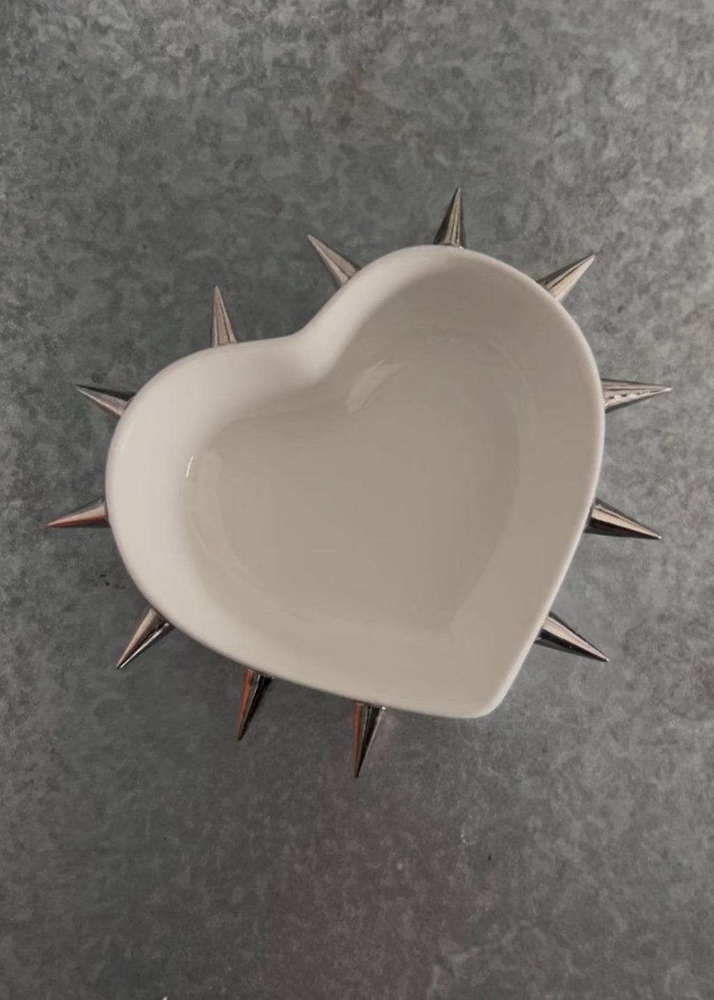 White heart ceramic bowl with spikes attached on a gray metal background 