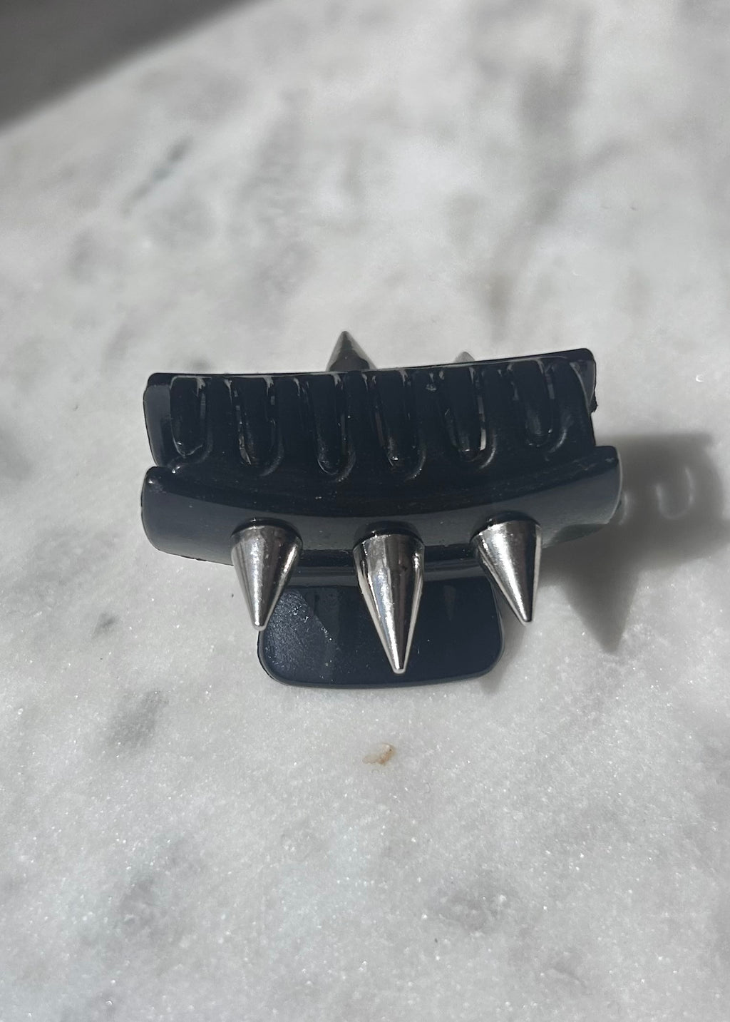Black hair clip with silver spikes on a textured white background
