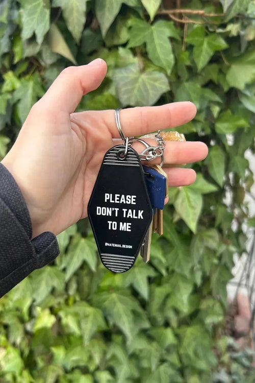 Hand holding black motel-style keychain that reads “Please don’t talk to me”