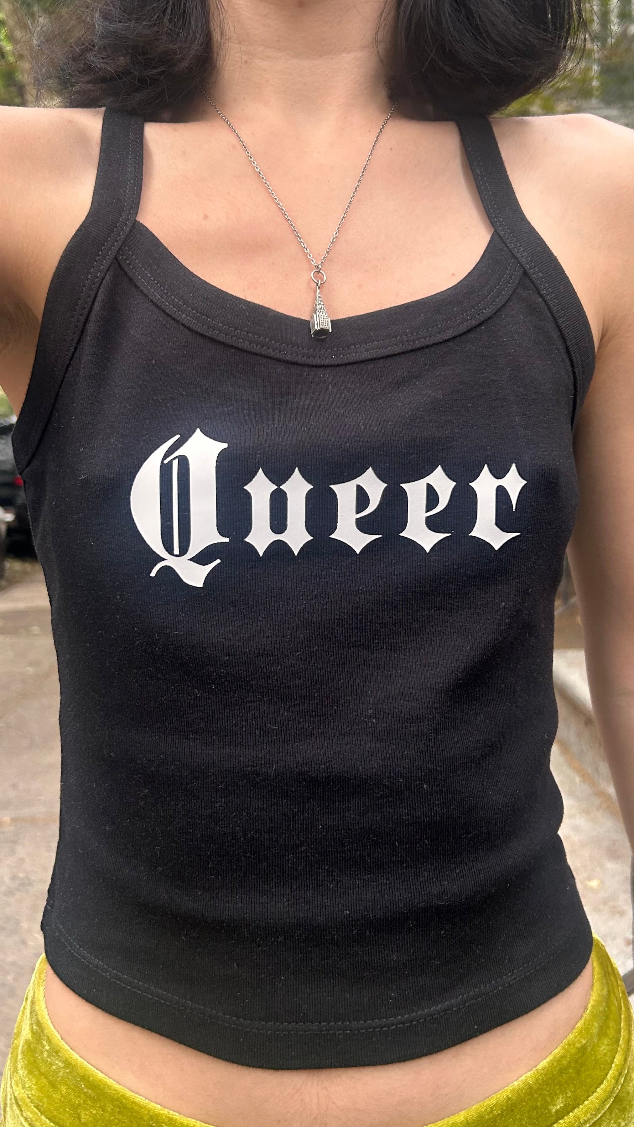 Person wearing a black tank top with 'Queer' printed on it.