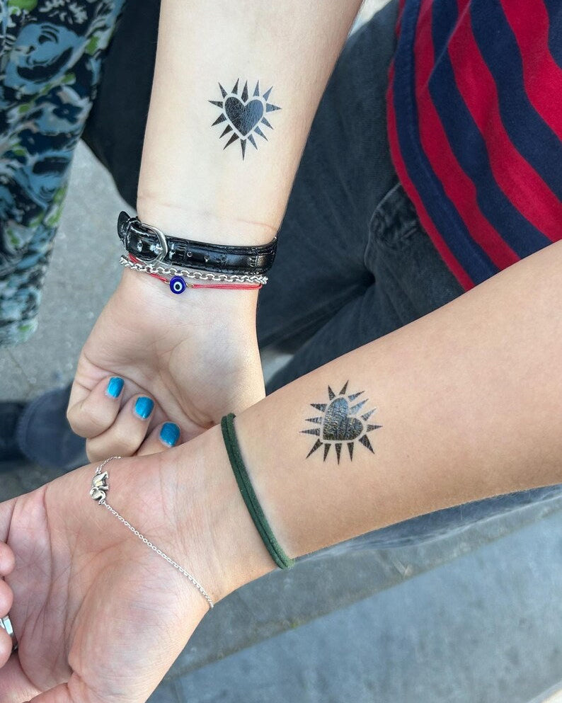 Two people’s forearms with black spiky heart temporary tattoos 