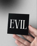 Hand holding a black square with 'EVIL' in white text against a gray background