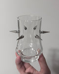 Clear glass vase with metallic spikes held against a plain background