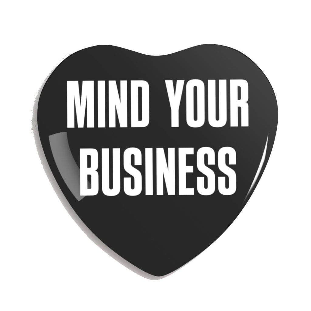 Black heart-shaped pin with 'MIND YOUR BUSINESS' text on a white background