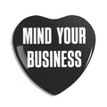 Black heart-shaped pin with 'MIND YOUR BUSINESS' text on a white background