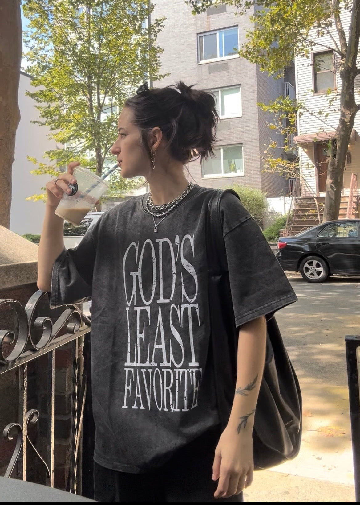 Person wearing a t-shirt with 'GOD'S LEAST FAVORITE' text, standing outdoors.