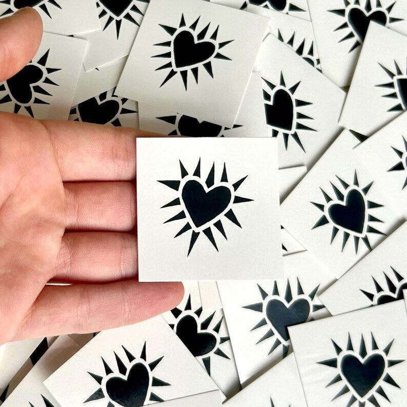 Hand holding black spiky heart temporary tattoo over a pile 