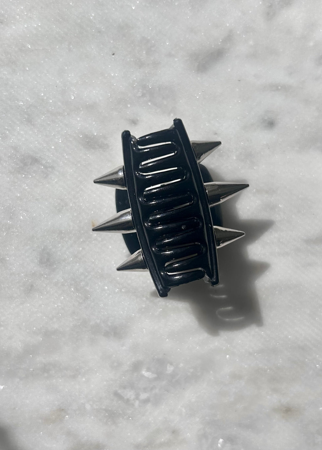 Black spiked hair clip on a gray marble surface
