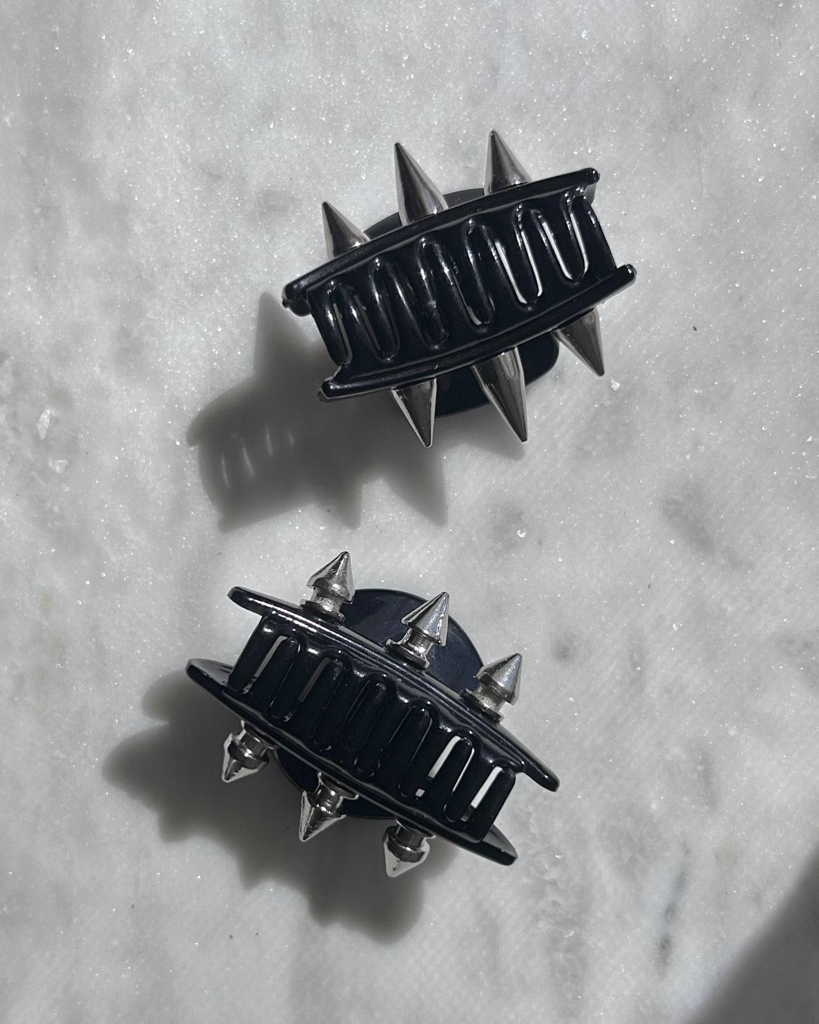 Black hair clips with spikes on a textured white surface