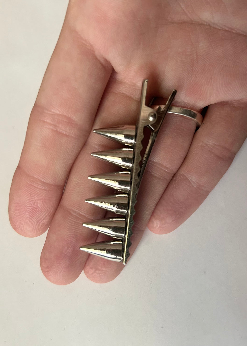 Metallic spiked hair clip on a hand against a plain background