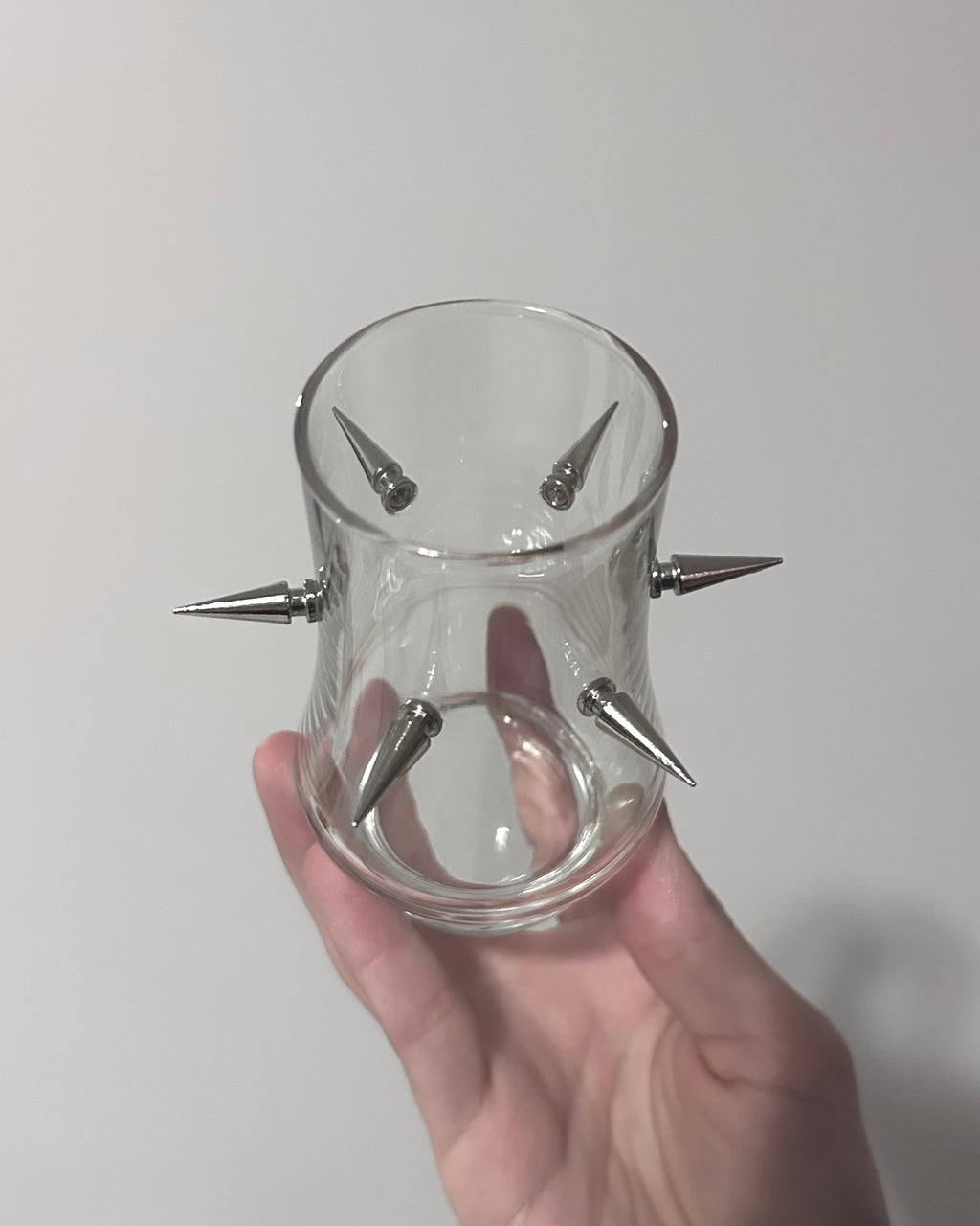 Clear glass container with spikes held by a hand against a plain background