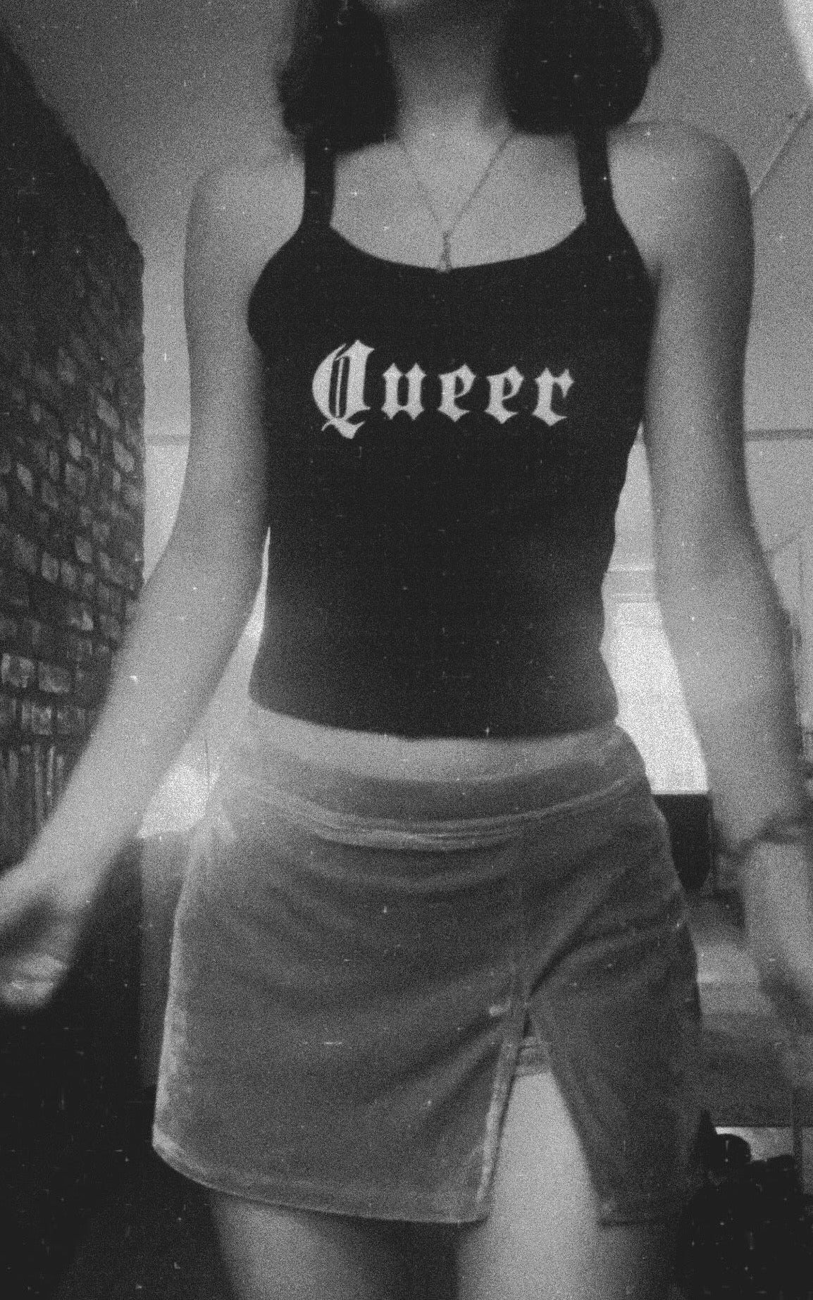 Person wearing a skirt and tank top that reads “QUEER”