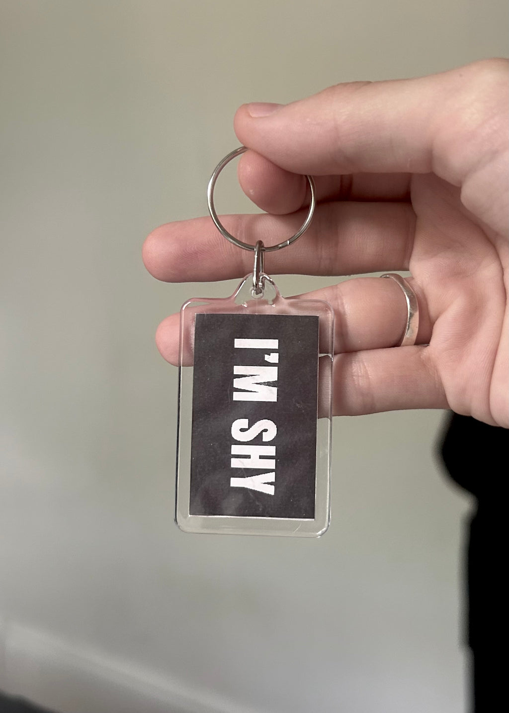 Hand holding a keychain with a clear tag displaying 'I'M SHY' text.