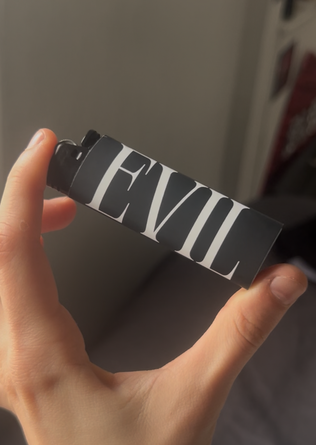 Hand holding a black lighter with 'EVIL' written on it against a neutral background