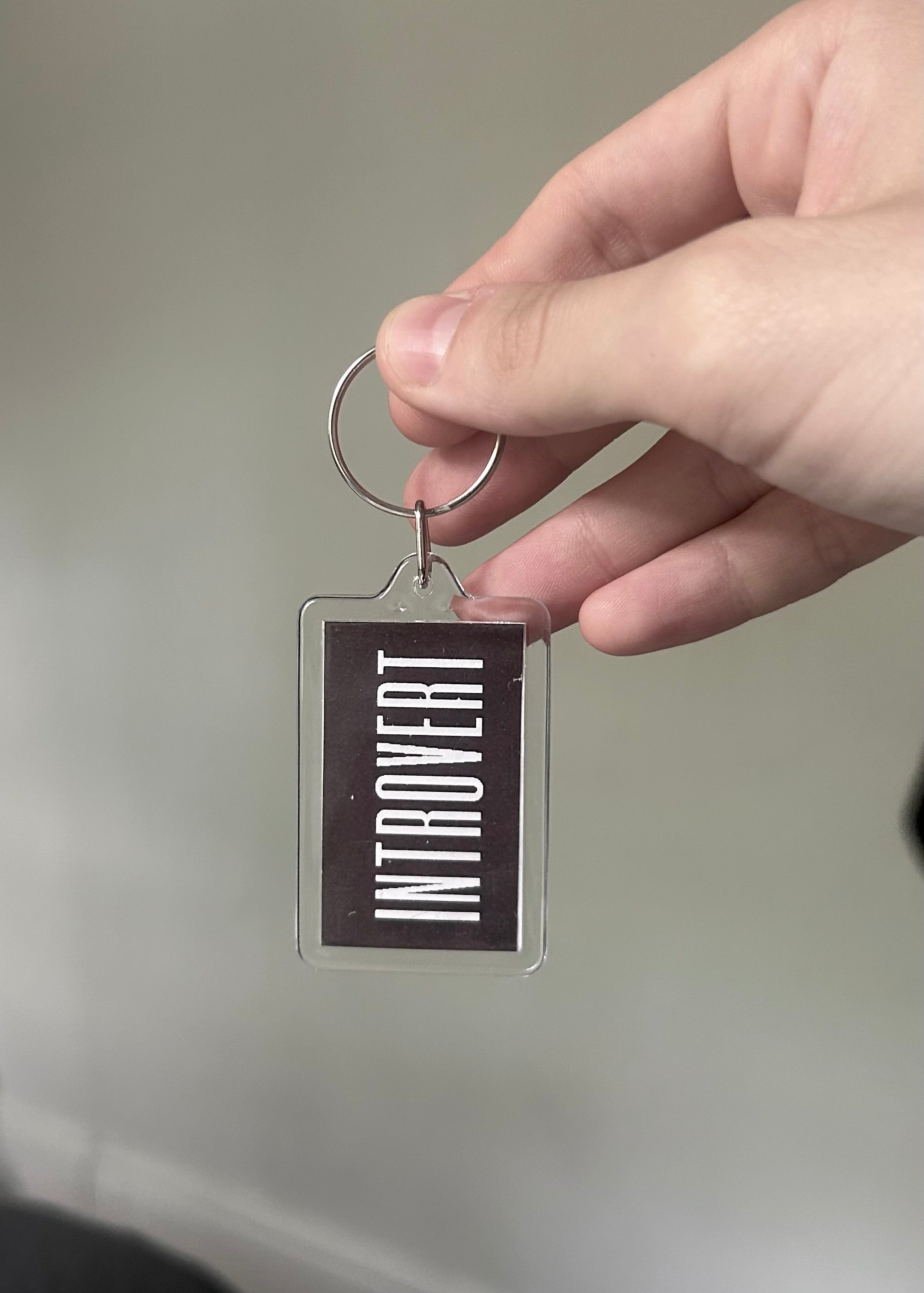 Hand holding a keychain with 'INTROVERT' text against a neutral background