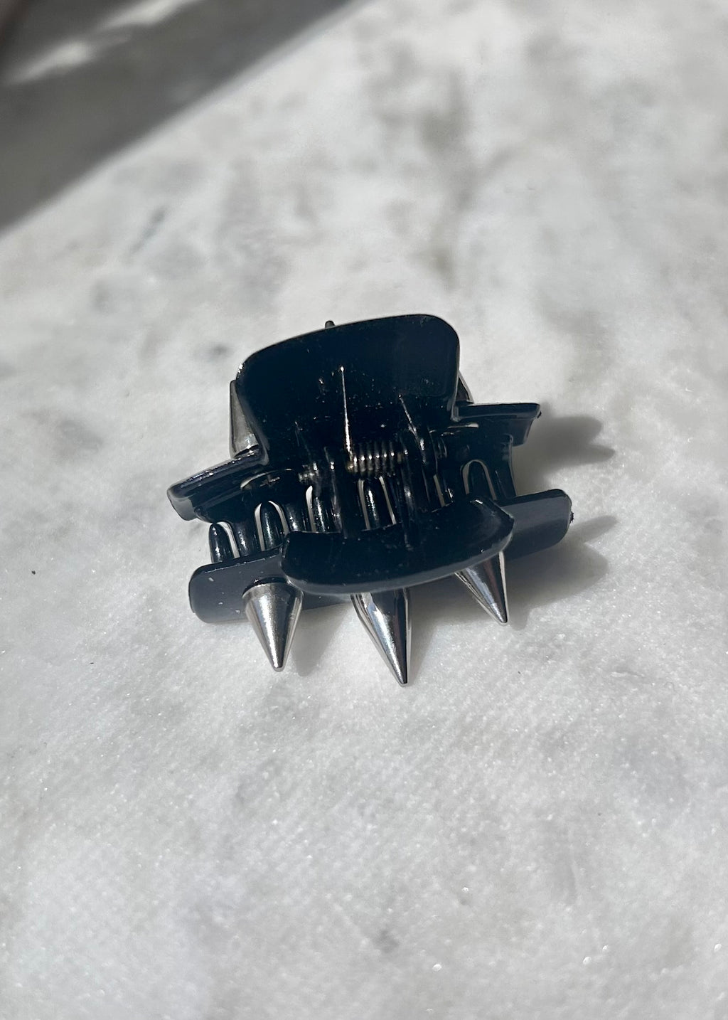 Black hair clip with spikes on a textured white surface