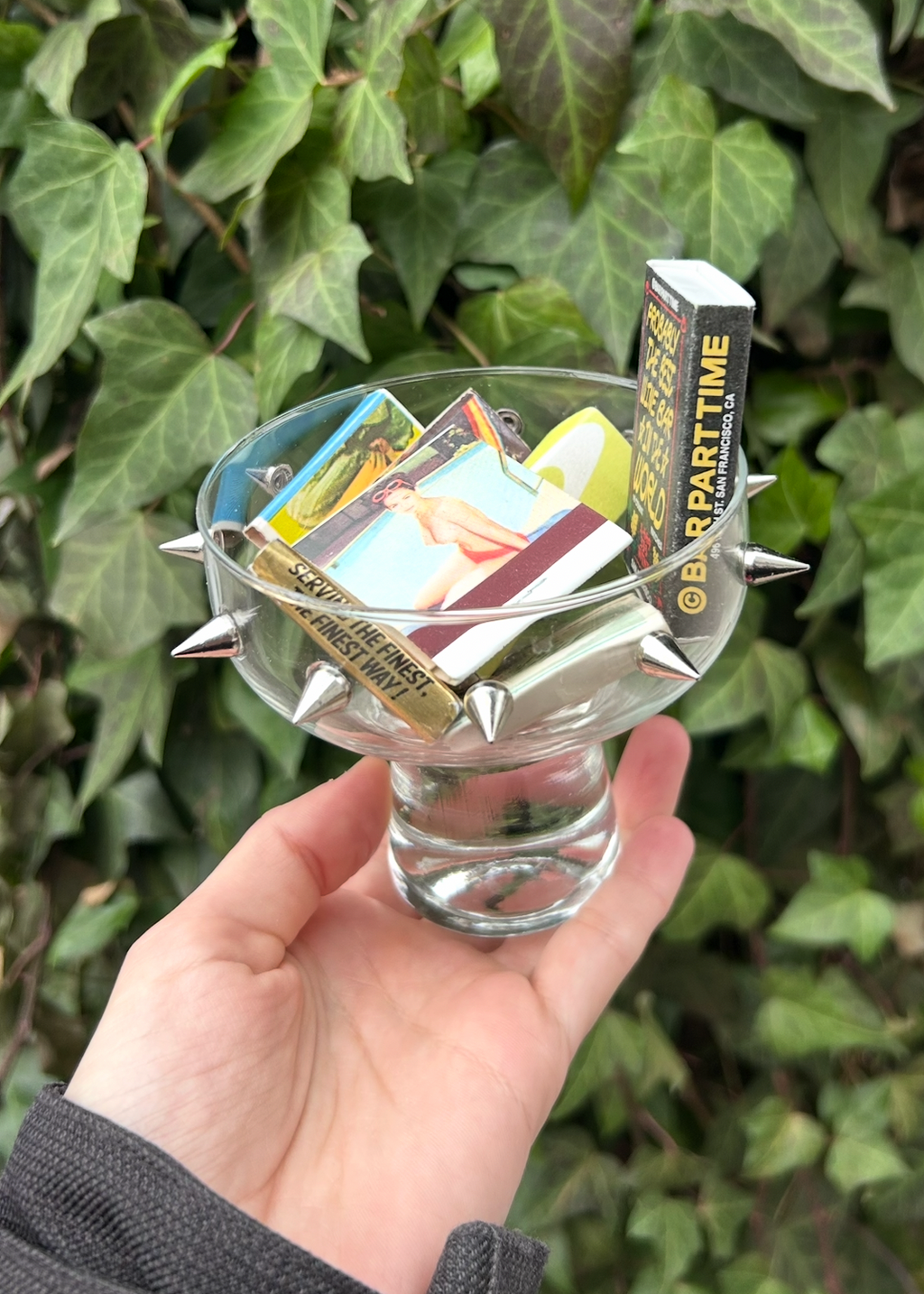 Hand holding a glass with matches against a green leafy background