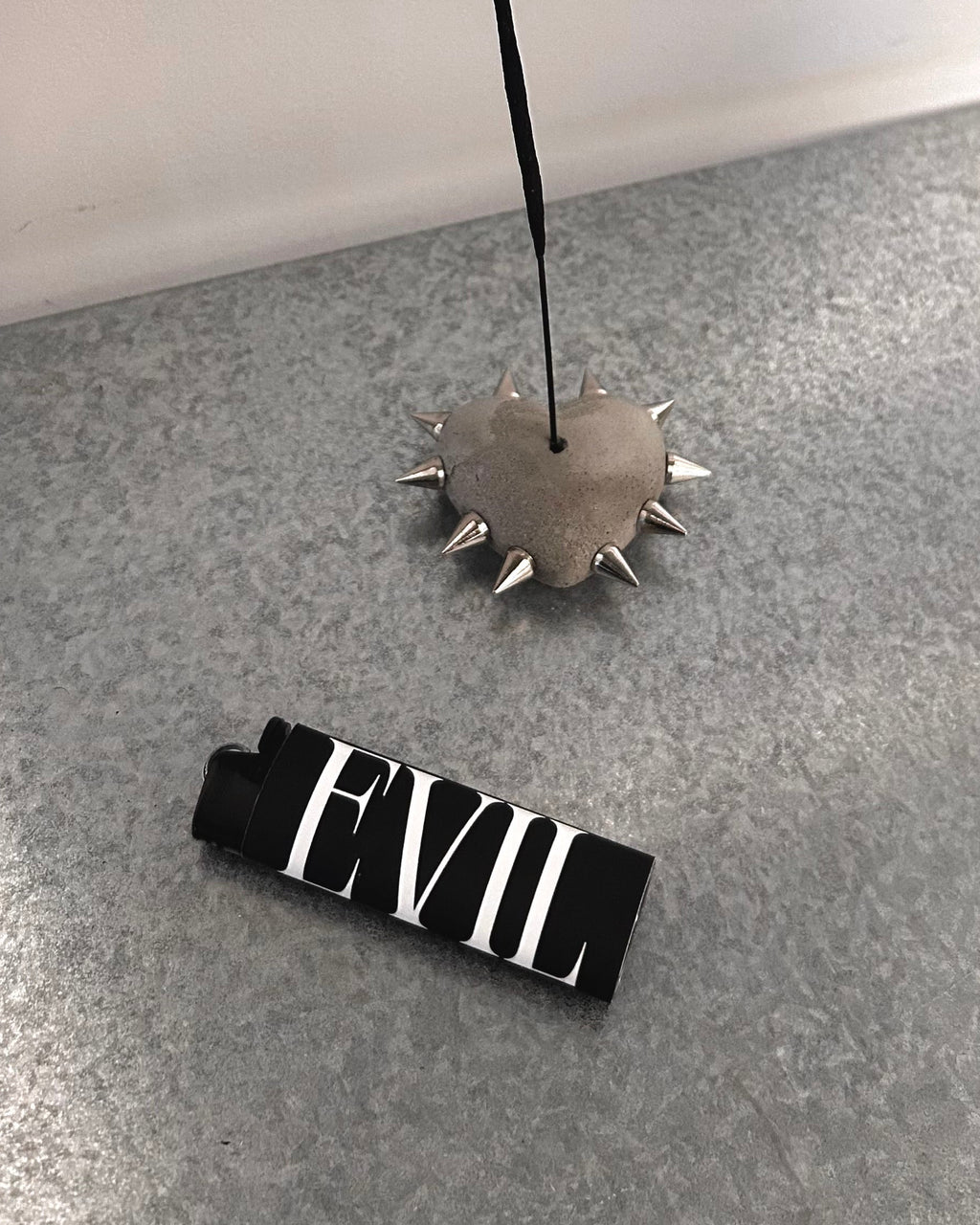 Metallic spiked incense holder and 'EVIL' lighter on a gray surface.