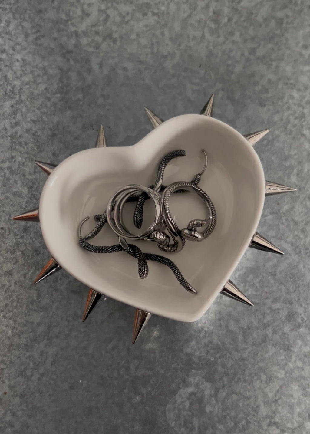 Heart-shaped bowl with spiky rim containing metallic rings on a gray textured background