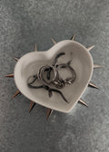 Heart-shaped bowl with spiky rim containing metallic rings on a gray textured background