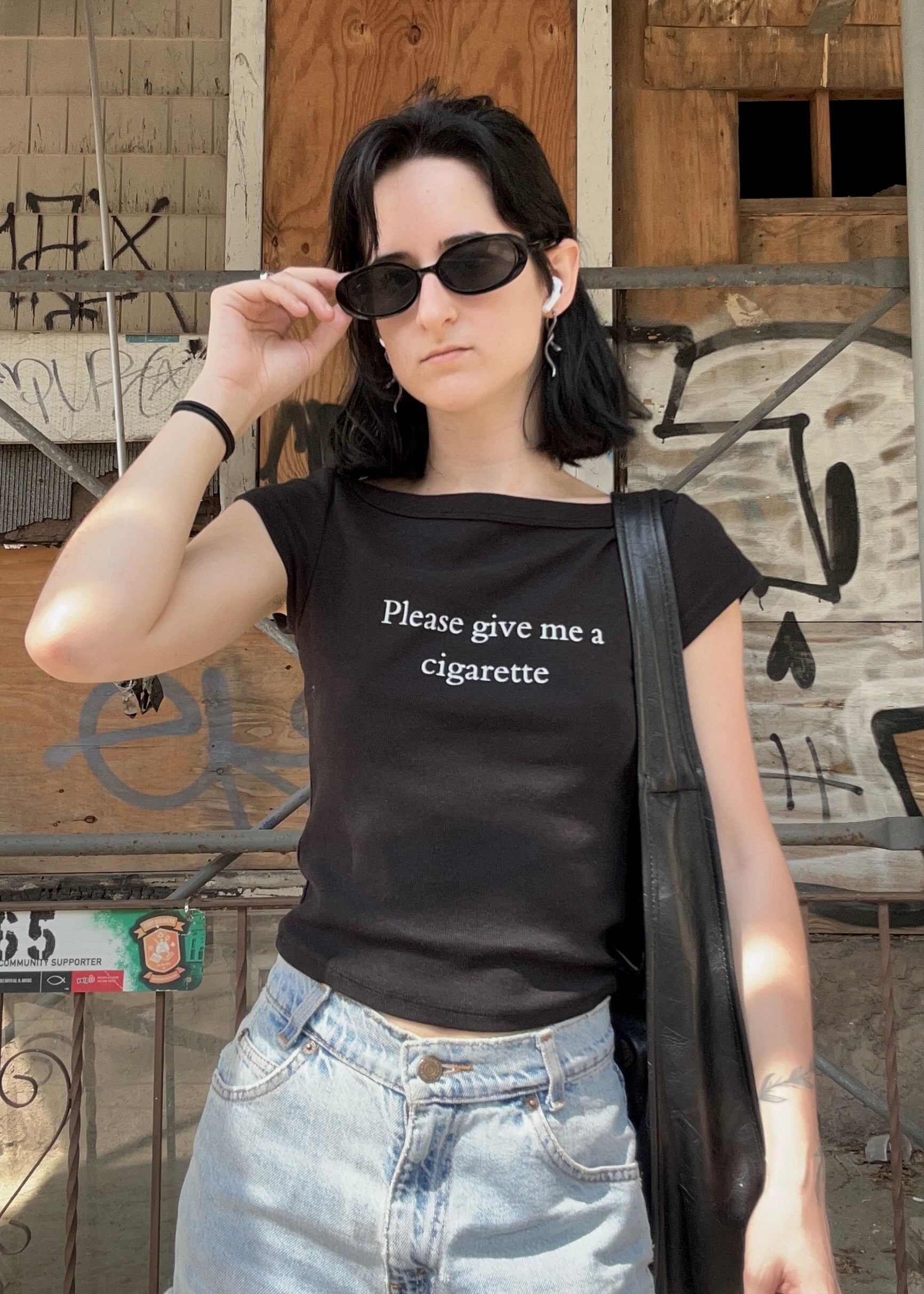 Person wearing a black t-shirt with text, standing in front of a graffiti-covered wall.
