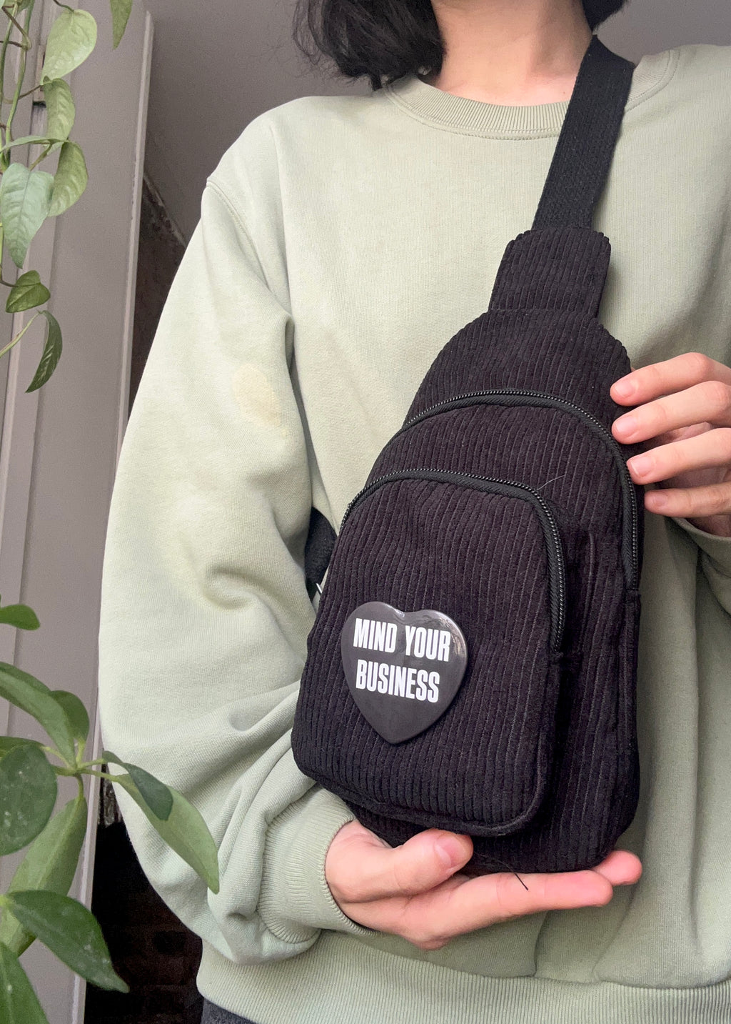Person holding a small black bag with a pin that reads “MIND YOUR BUSINESS”