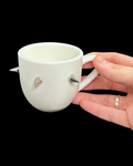 White ceramic cup with spike designs held by a hand against a black background