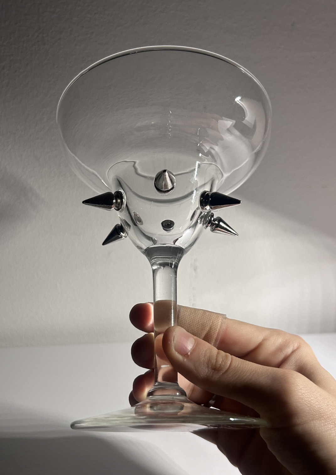 Clear glass with spikes held by a hand against a neutral background